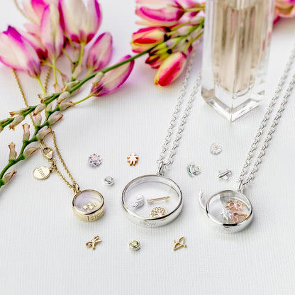 Stow lockets on a white surface with pink flowers in the background and charms