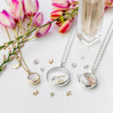Stow lockets on a white surface with pink flowers in the background and charms