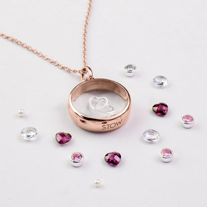 Rose gold necklace with heart-shaped locket and surrounding gemstones on a light background